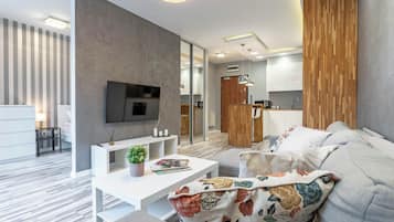 A modern living room with a flat-screen TV, a white console table, and a sofa with floral cushions.