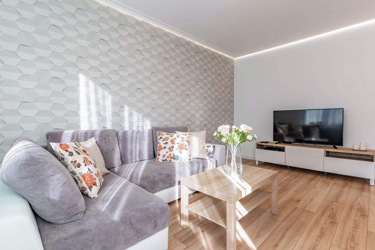 A modern living room with a grey sofa, a coffee table, and a flat-screen TV on a wooden cabinet.