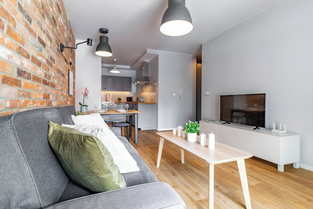Una sala moderna con un sofá gris, una mesa de centro de madera y un televisor sobre un mueble blanco.