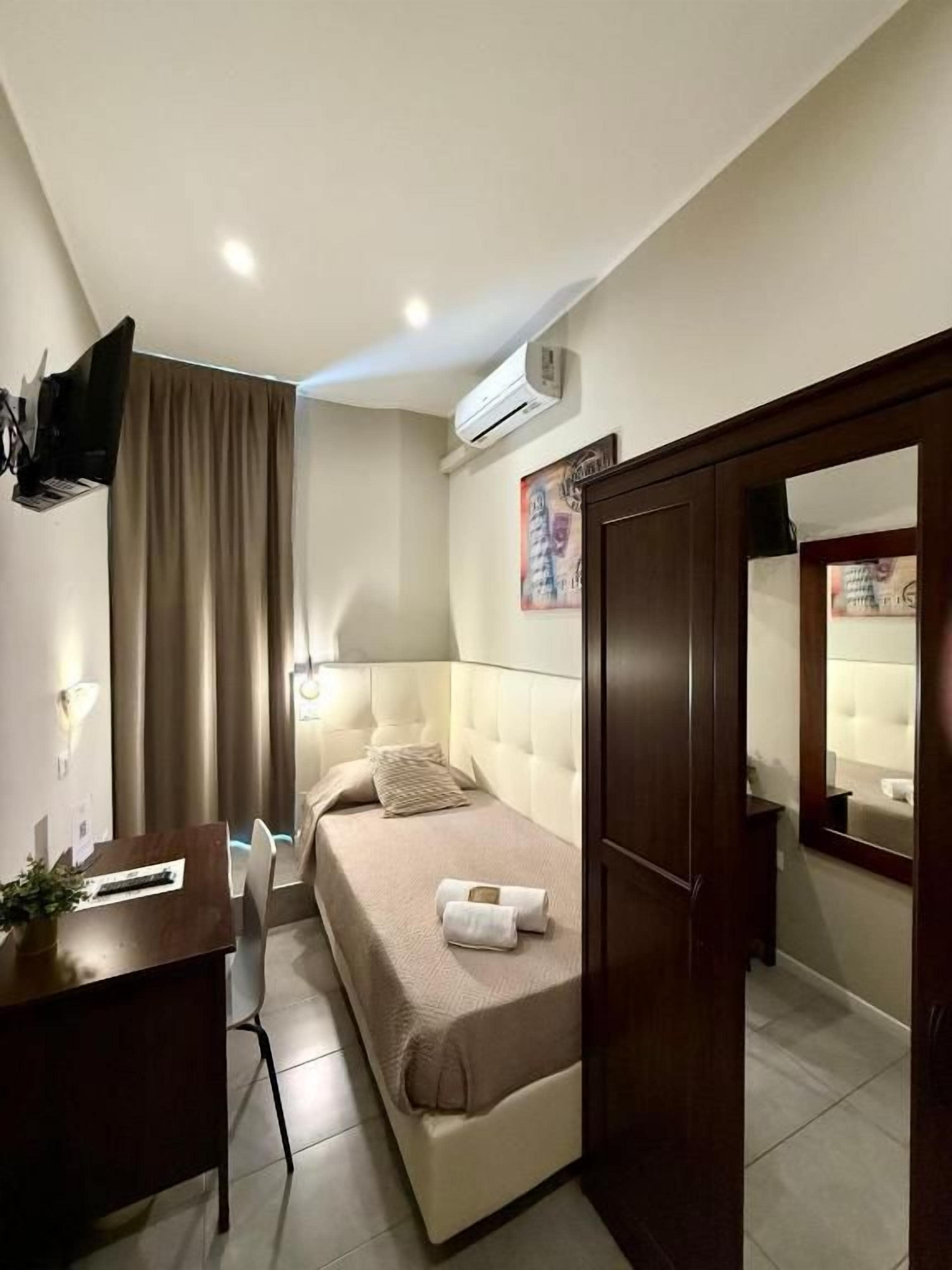 Habitación de hotel con cama, escritorio, silla, equipo de aire acondicionado y televisor montado en la pared.