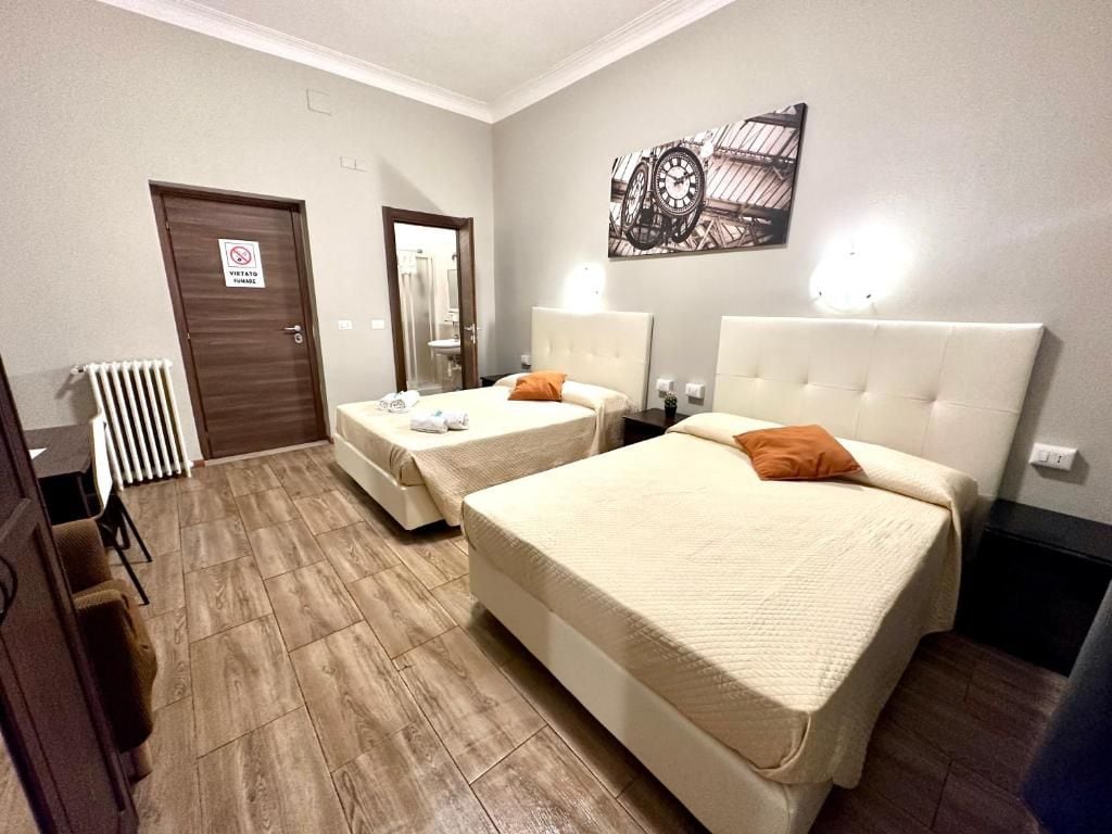 A hotel room with two beds, a radiator, a door with a sign, and a wall-mounted clock.