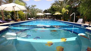 Una piscina con sillas de descanso y sombrillas, rodeada de follaje.