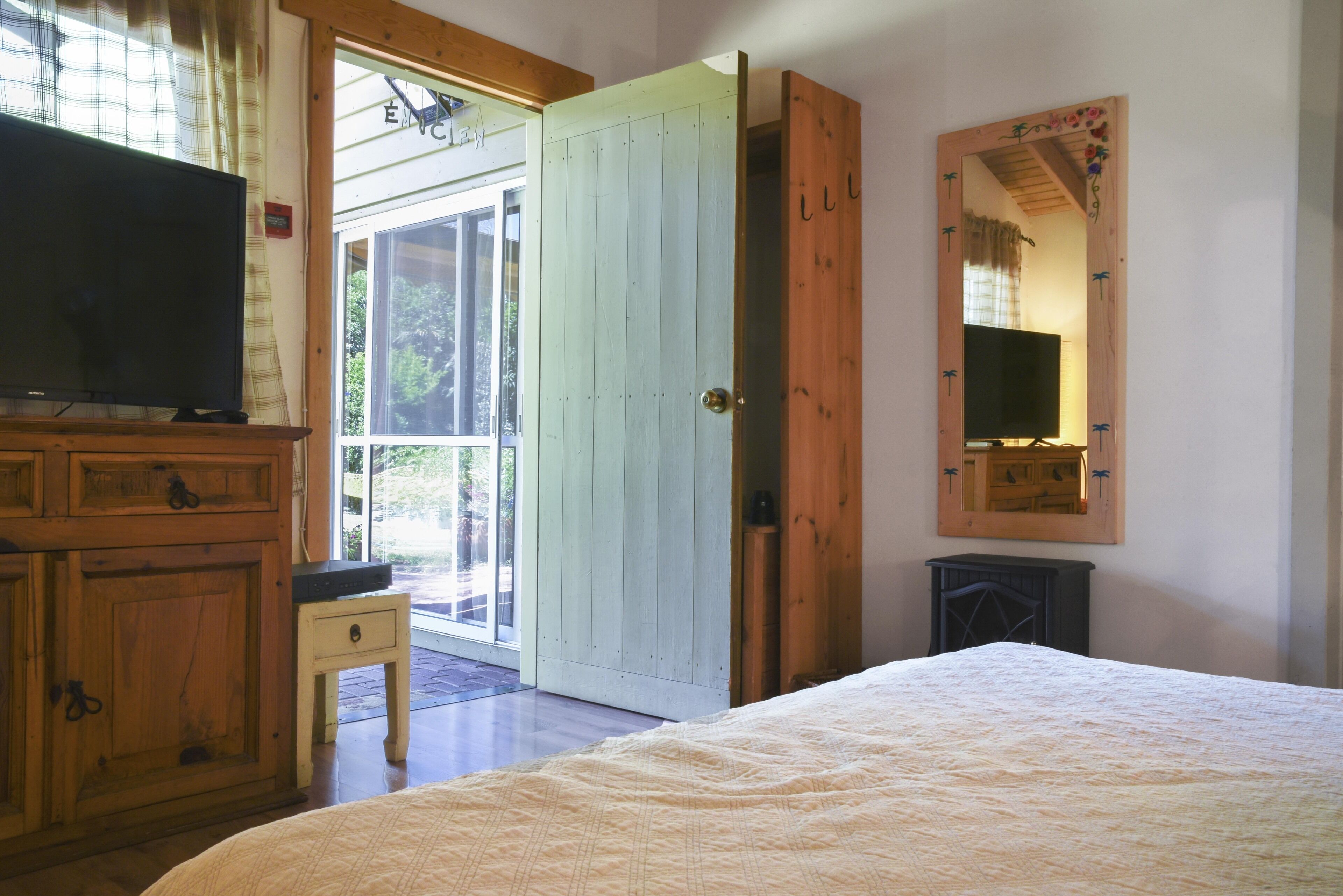 A bedroom with a bed, a television, a wooden cabinet, and a sliding glass door leading to an outdoor area.