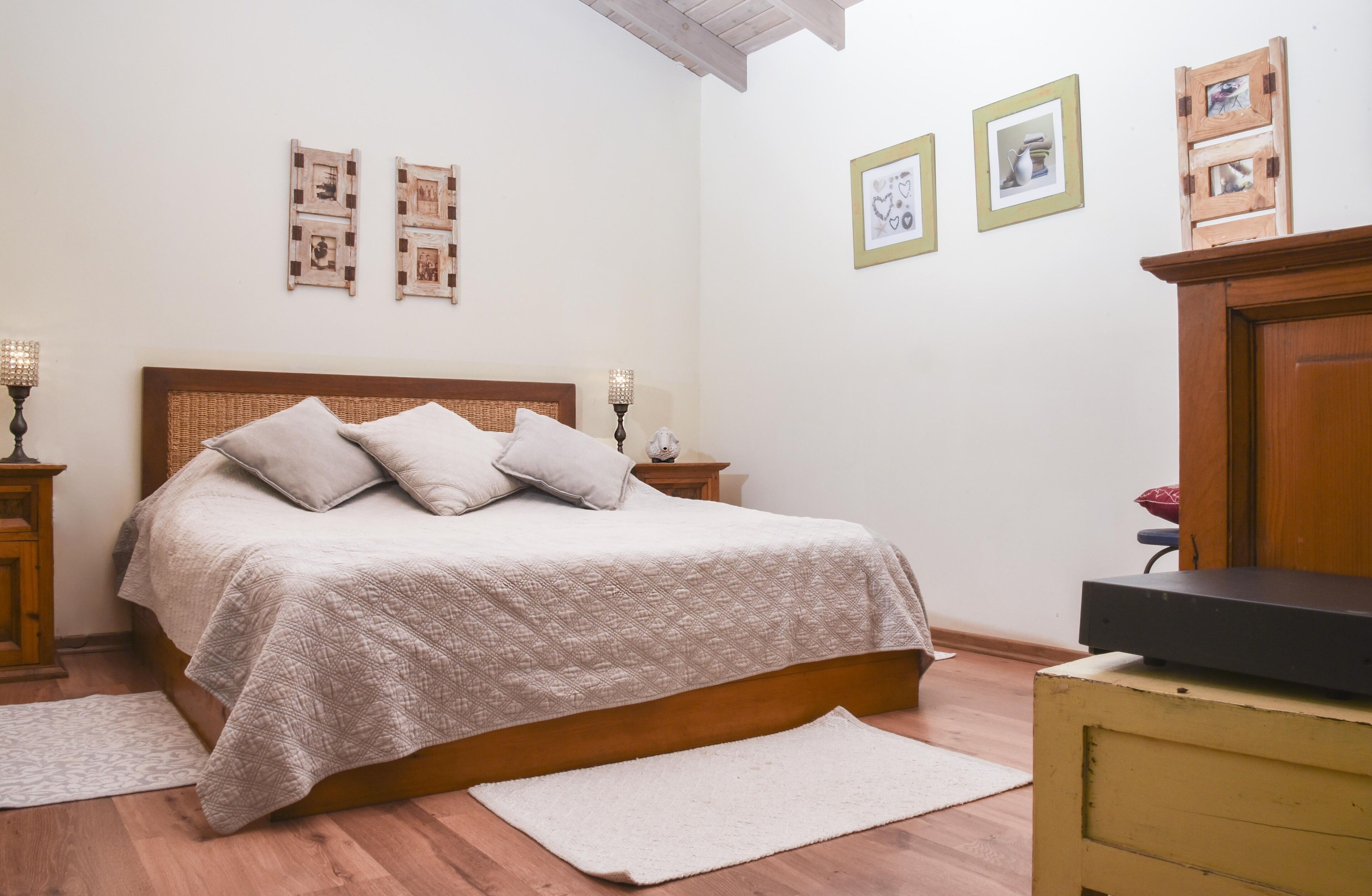 A bedroom with a wooden bed, a nightstand, a dresser, and a wall with framed pictures.