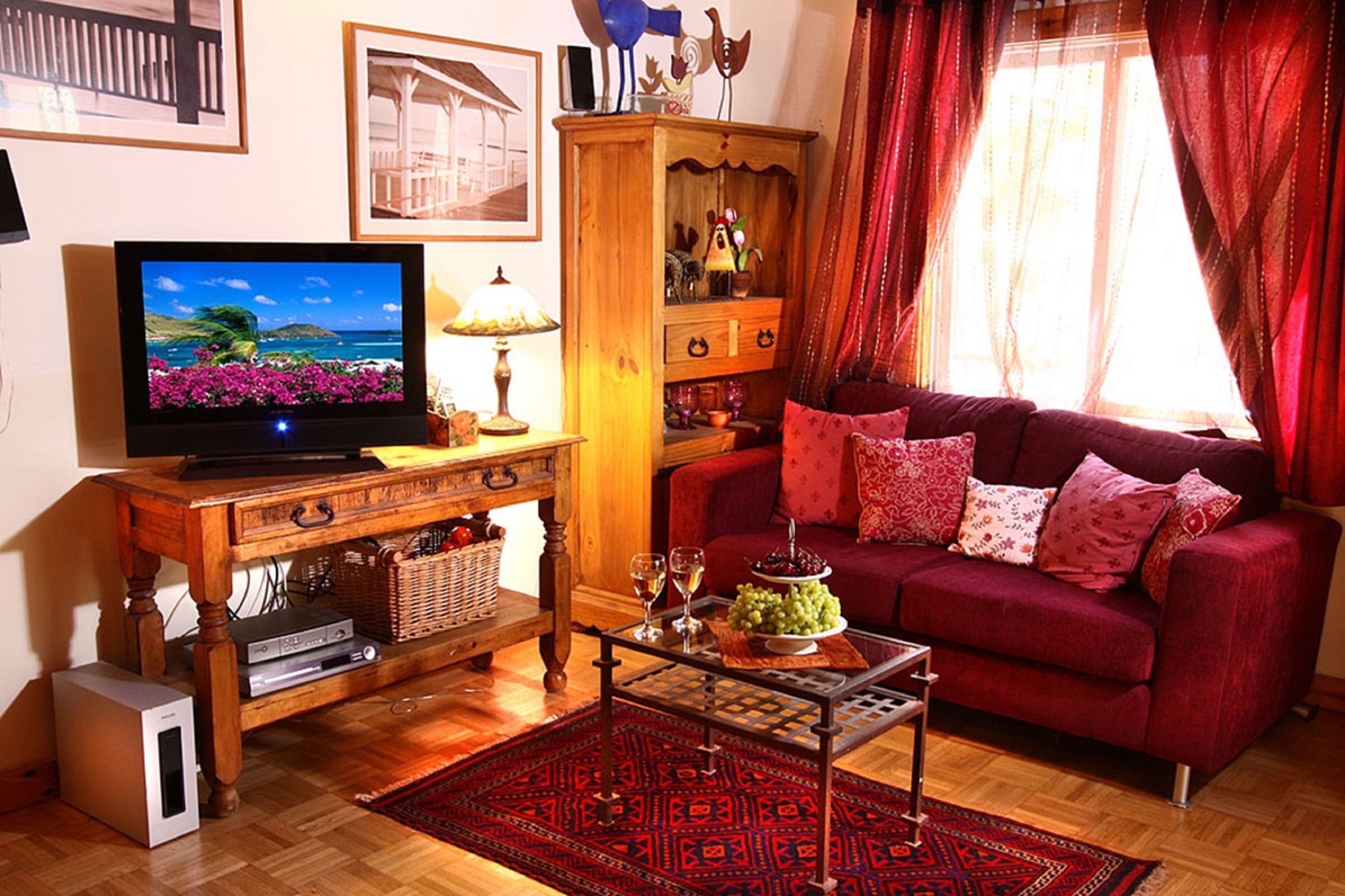 A living room with a television, a wooden cabinet, a red sofa, and a patterned rug.