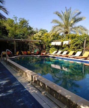 A swimming pool with lounge chairs and a covered area, surrounded by palm trees and greenery. - Beit Ram Sherf Country Resort (Ramot)
