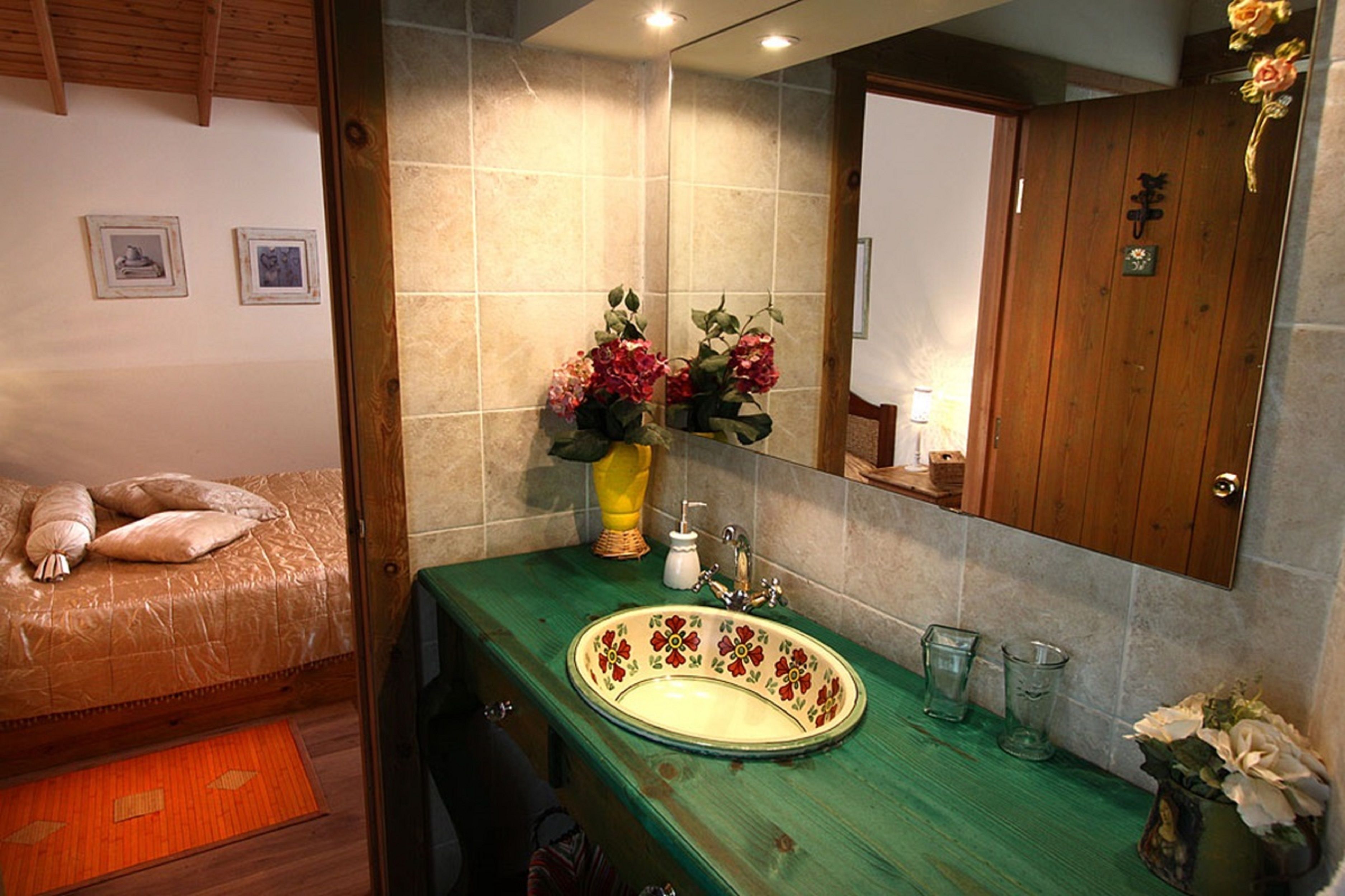 A bathroom with a green countertop, a sink with floral designs, a mirror, and a bed with a wooden headboard.