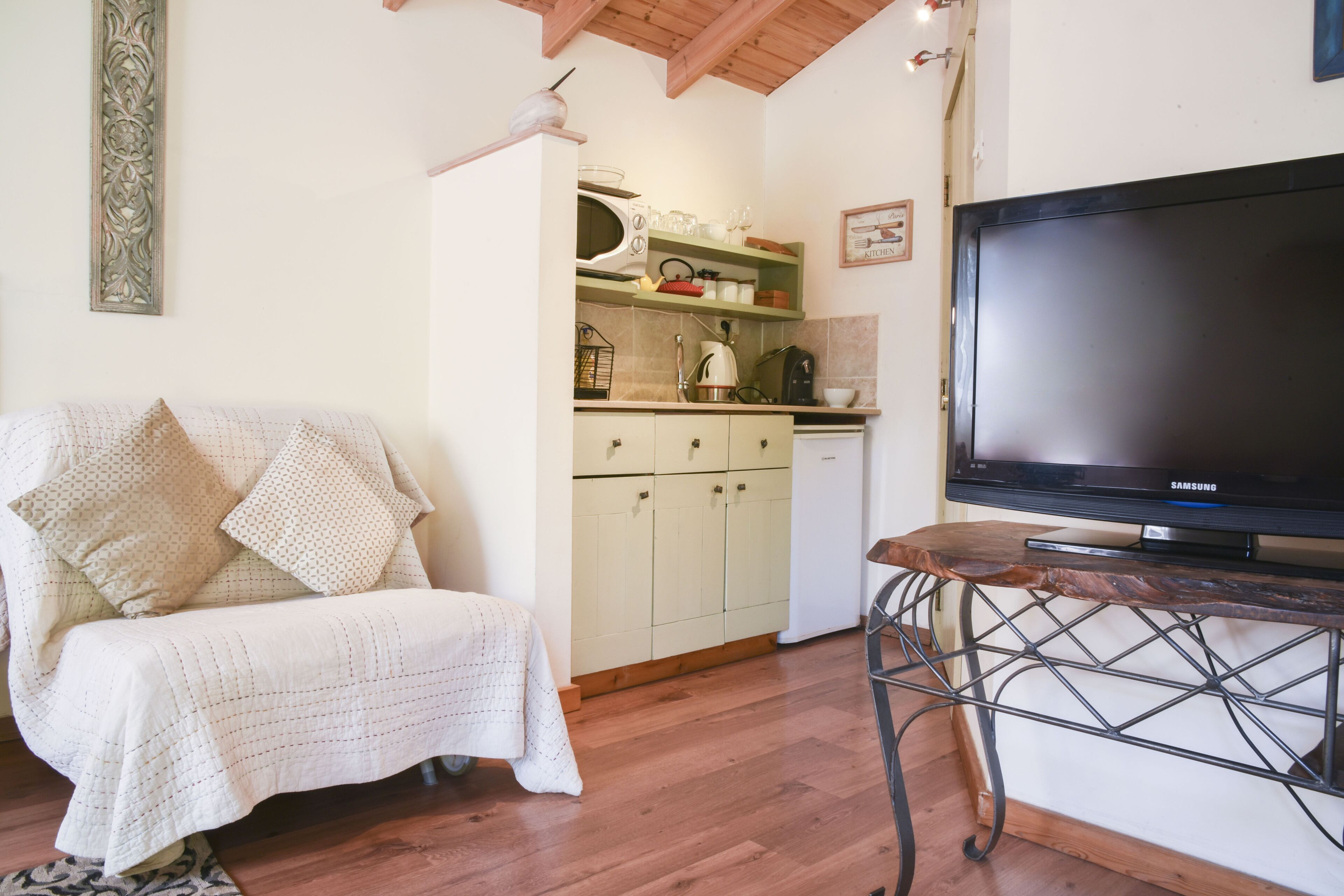 A cozy living area with a sofa, a television on a stand, and a kitchen in the background.