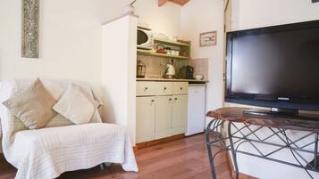 A cozy living area with a sofa, a television on a stand, and a kitchen in the background.