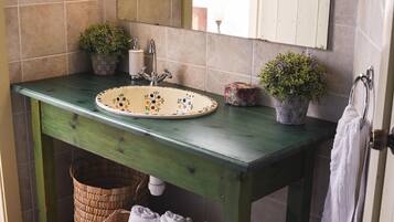 A bathroom with a green vanity, a sink with floral designs, two potted plants, a white towel, and a mirror above the sink.