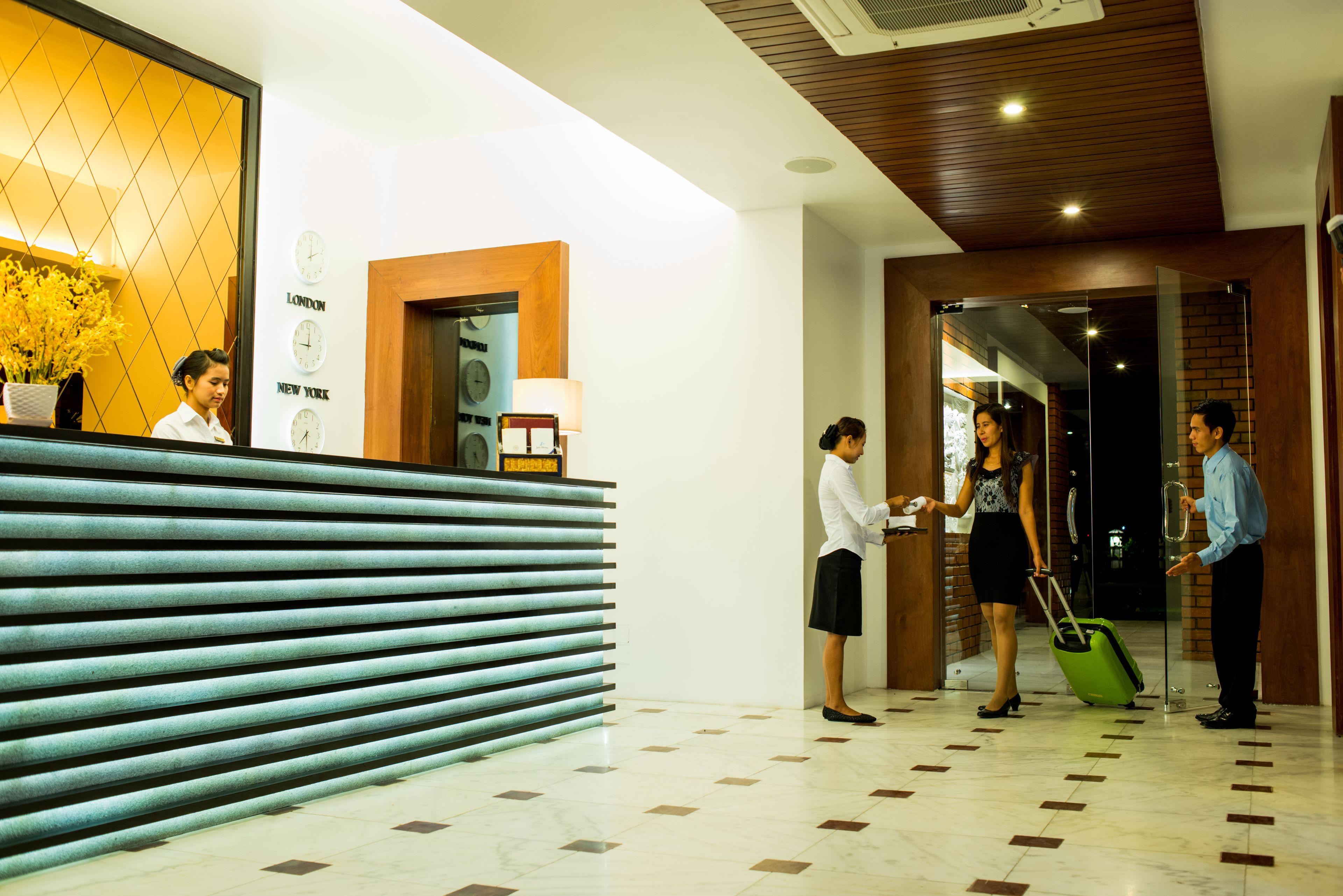 Zona de recepción de hotel con mostrador, un reloj y una pared con nombres de ciudades.