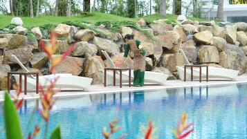 A pool area with a waterfall feature, lounge chairs, and a person tending to the water feature.