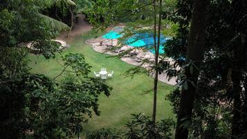 A lush, green outdoor area with a swimming pool, surrounded by trees and a small patio with a table and chairs.