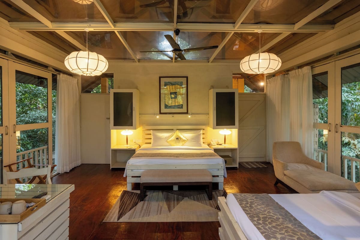 Ein Schlafzimmer mit einem großen Bett, Nachttischlampen, einem Deckenventilator und Blick auf Grün hinter den Fenstern.
