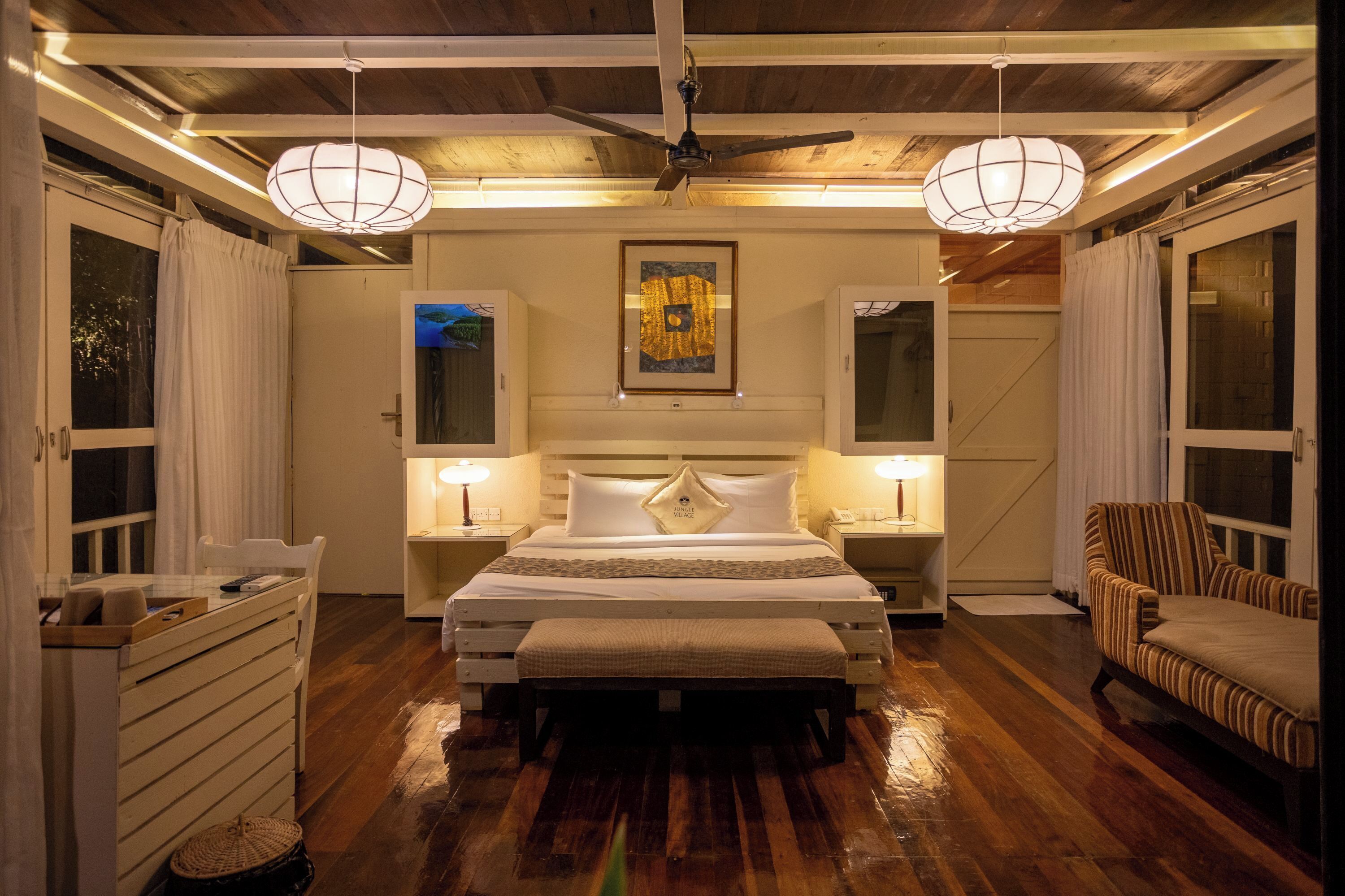 A bedroom with a bed, bedside tables, a chair, a ceiling fan, and a large window.