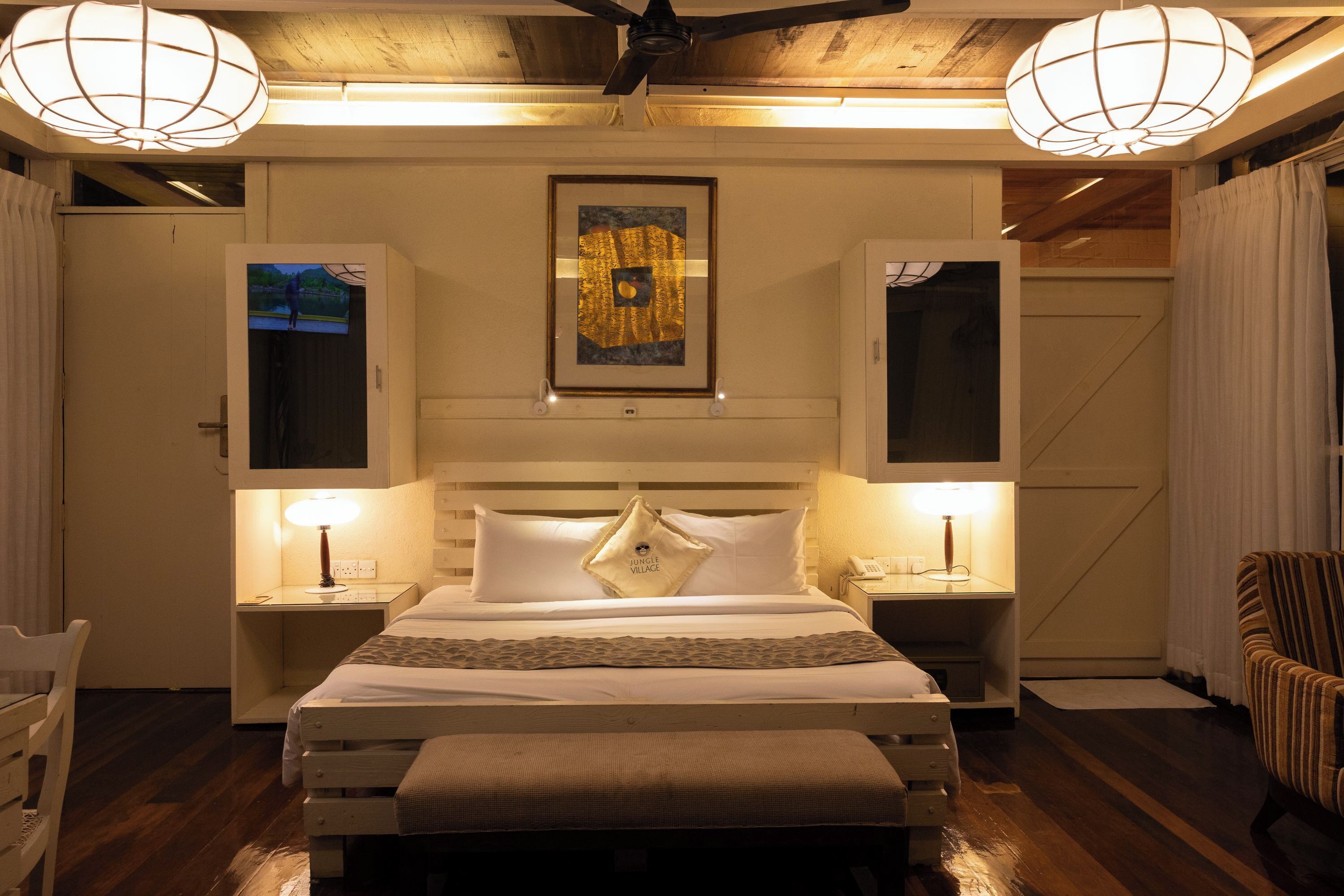 Una habitación de hotel con una cama grande, dos mesitas de noche, una silla y un ventilador de techo.
