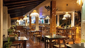 Un restaurant amb taules i cadires de fusta, llums penjants i una zona de bar.