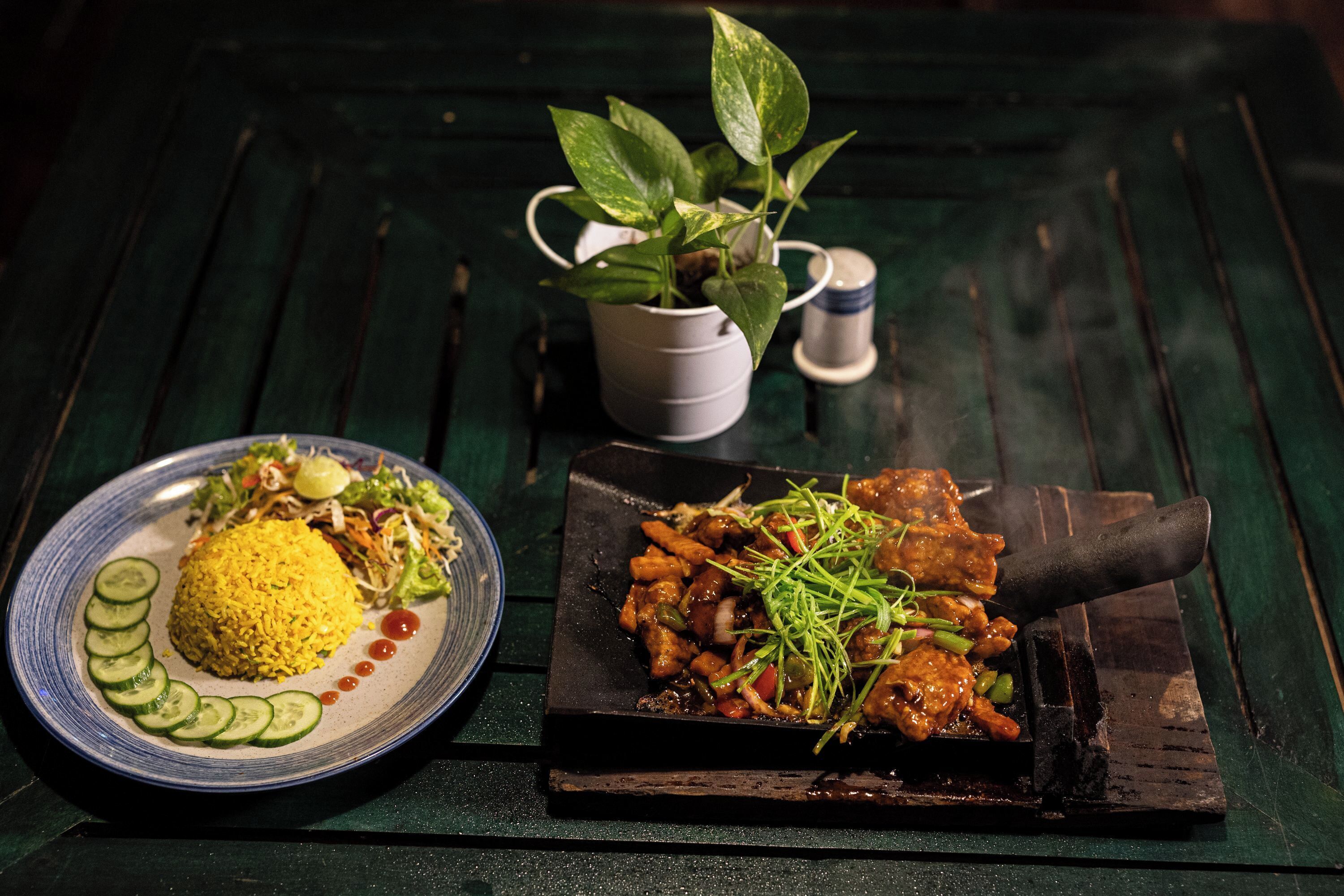Un plato de arroz amarillo, rodajas de pepino y una ensalada con una espátula negra sobre una mesa de madera.