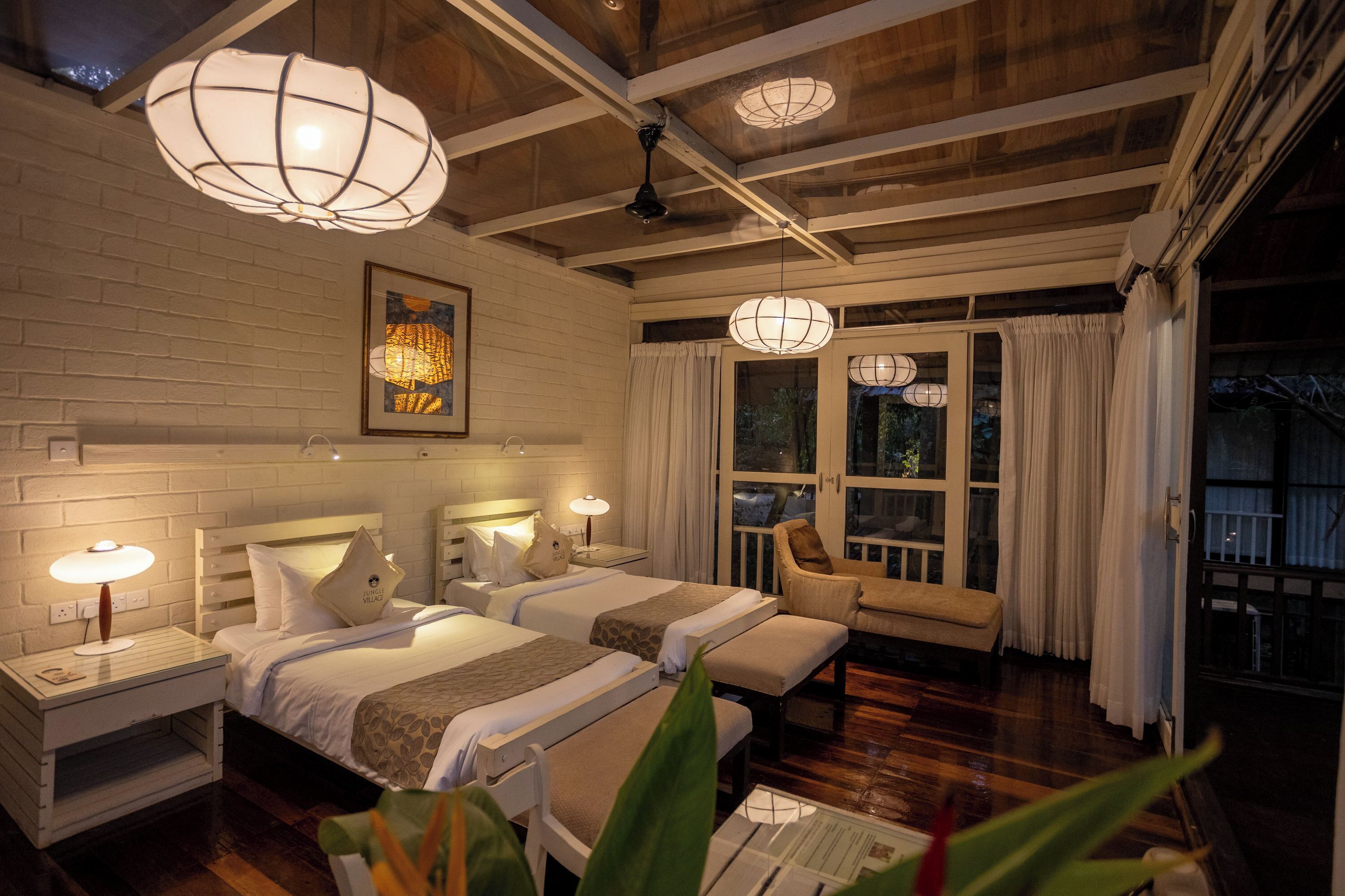 A hotel room with two beds, a sitting area, and a balcony with curtains.