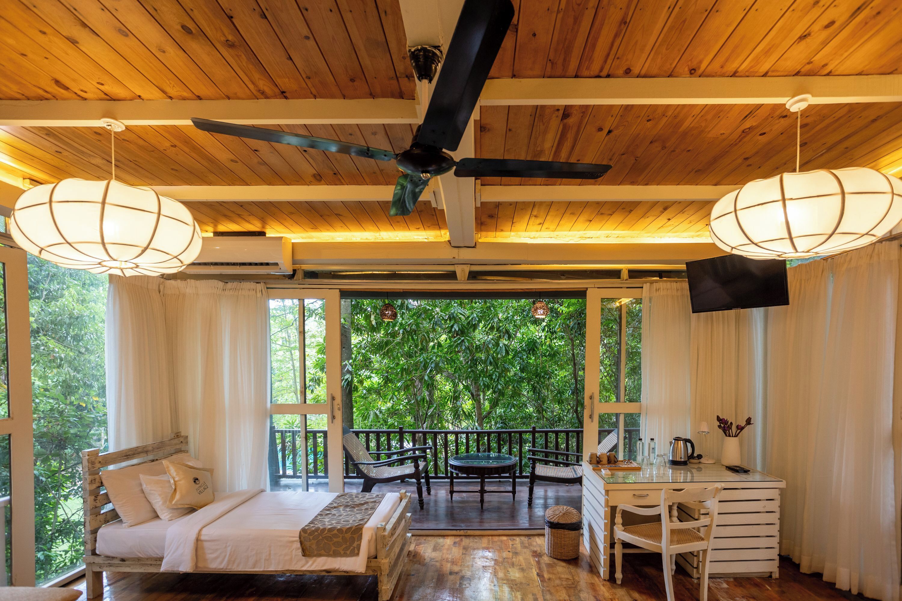 Un soffitto in legno con una ventola a soffitto, un letto con cuscini, un tavolo con sedie e vista sul verde all'esterno.