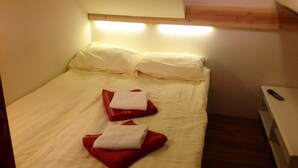 A small, neatly made bed with white linens and two red towels folded on top.