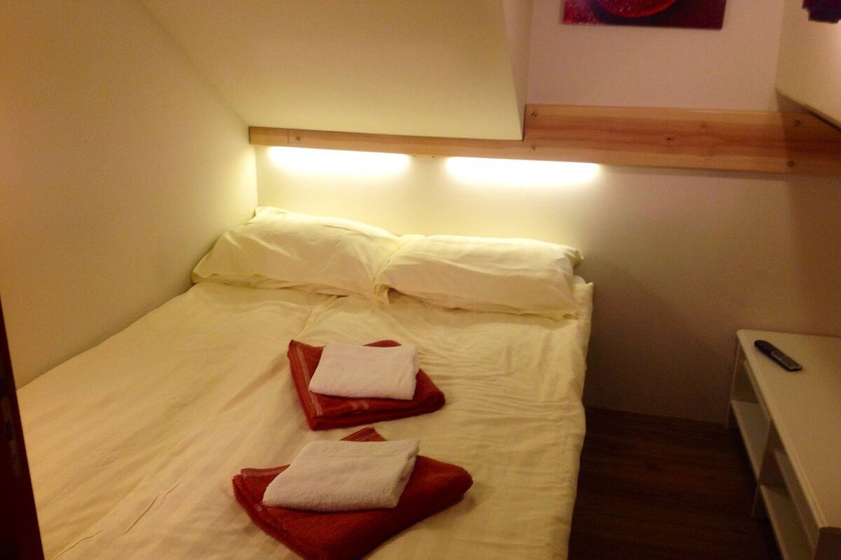 Un petit lit bien fait, avec des draps blancs et deux serviettes rouges pliées posées sur le dessus.