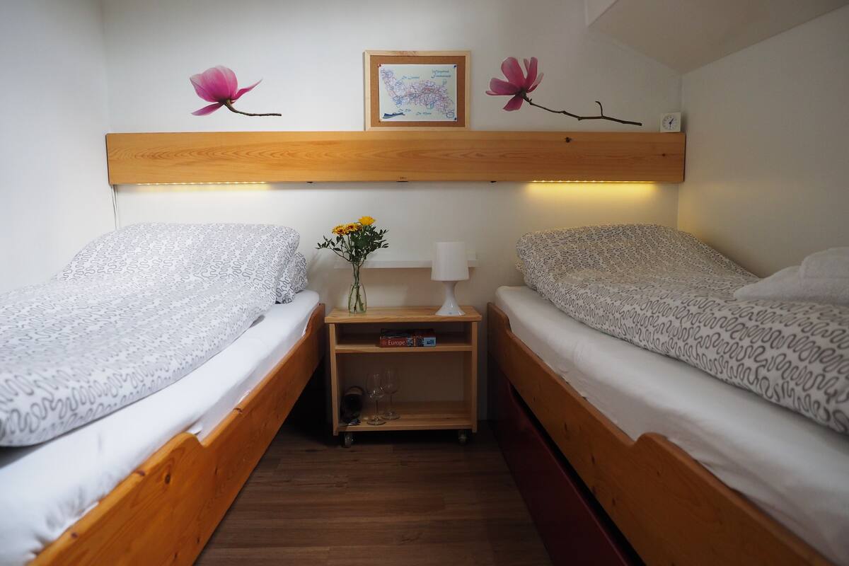 Une petite chambre accueillante, avec deux lits en bois, une table de chevet avec une lampe et une carte encadrée accrochée au mur.