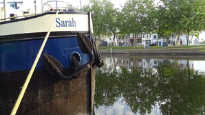 A boat named 'Sarah' docked near a canal with buildings and trees in the background. - Hotelschip Sarah (Amsterdam)