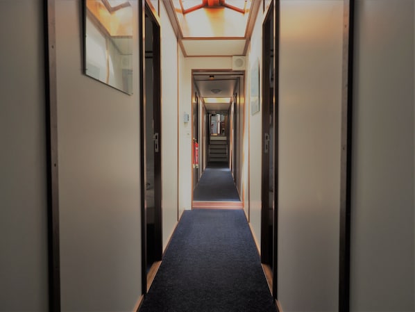 A narrow, well-lit hallway with a carpeted floor, leading to a door at the end. - Hotelschip Sarah (Amsterdam)