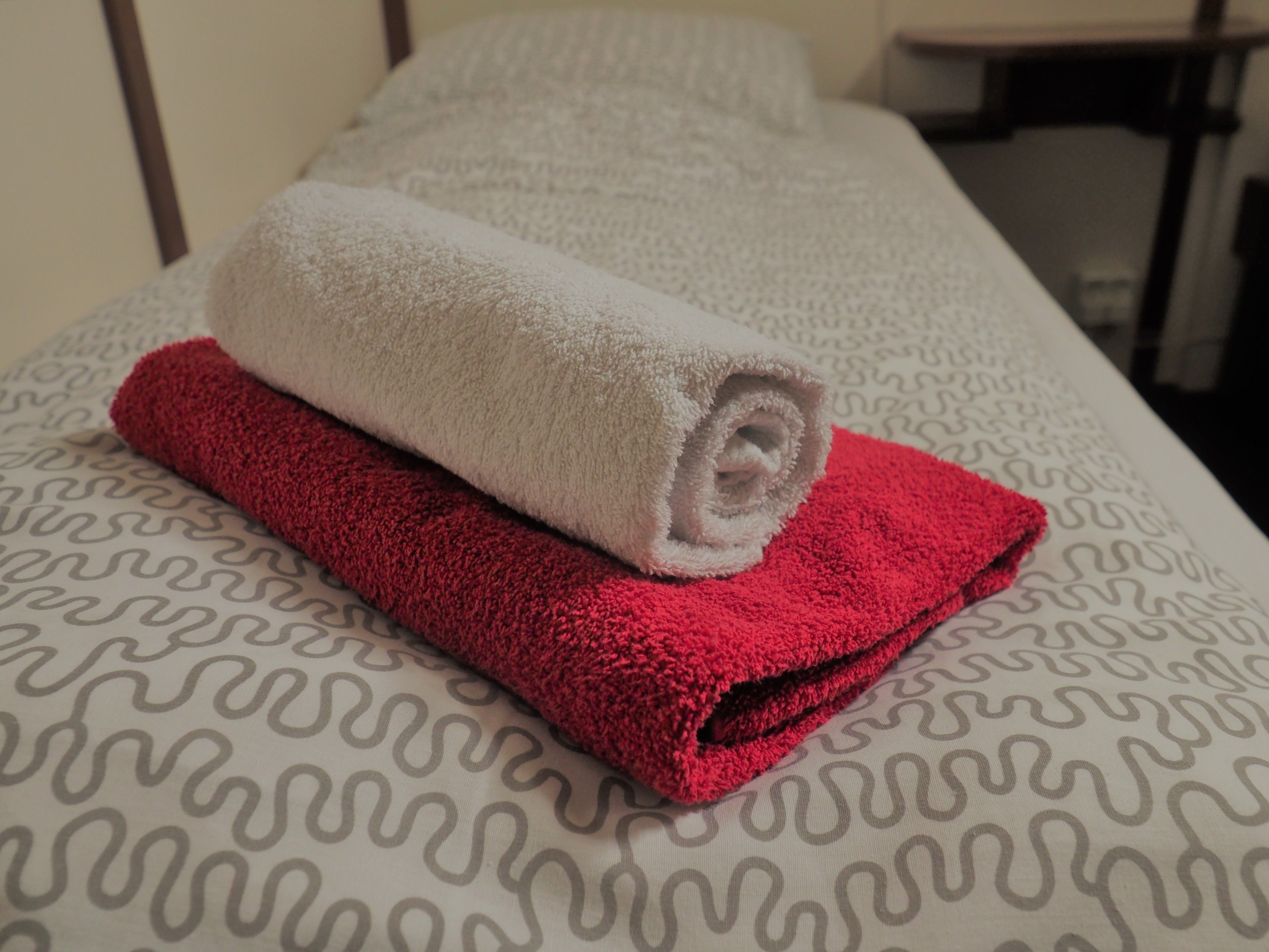 A bed with a patterned bedspread and two rolled towels, one white and one red.