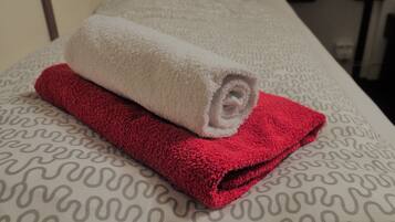 A bed with a patterned bedspread and two rolled towels, one white and one red.