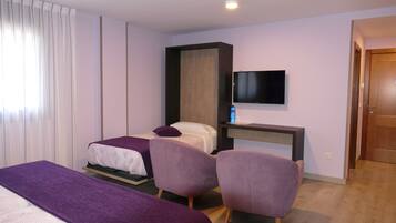A hotel room with a bed, two chairs, a TV, and a wooden desk.