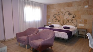 Une chambre à coucher avec un lit, deux fauteuils, une table de chevet et une fenêtre avec des rideaux.
