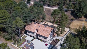Une maison à deux étages, avec un toit en tuiles, entourée d’une forêt dense.