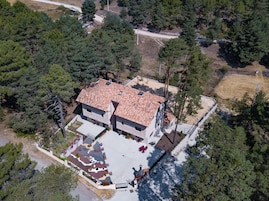 Una casa de dos pisos con techo de tejas, rodeada de un bosque frondoso.
