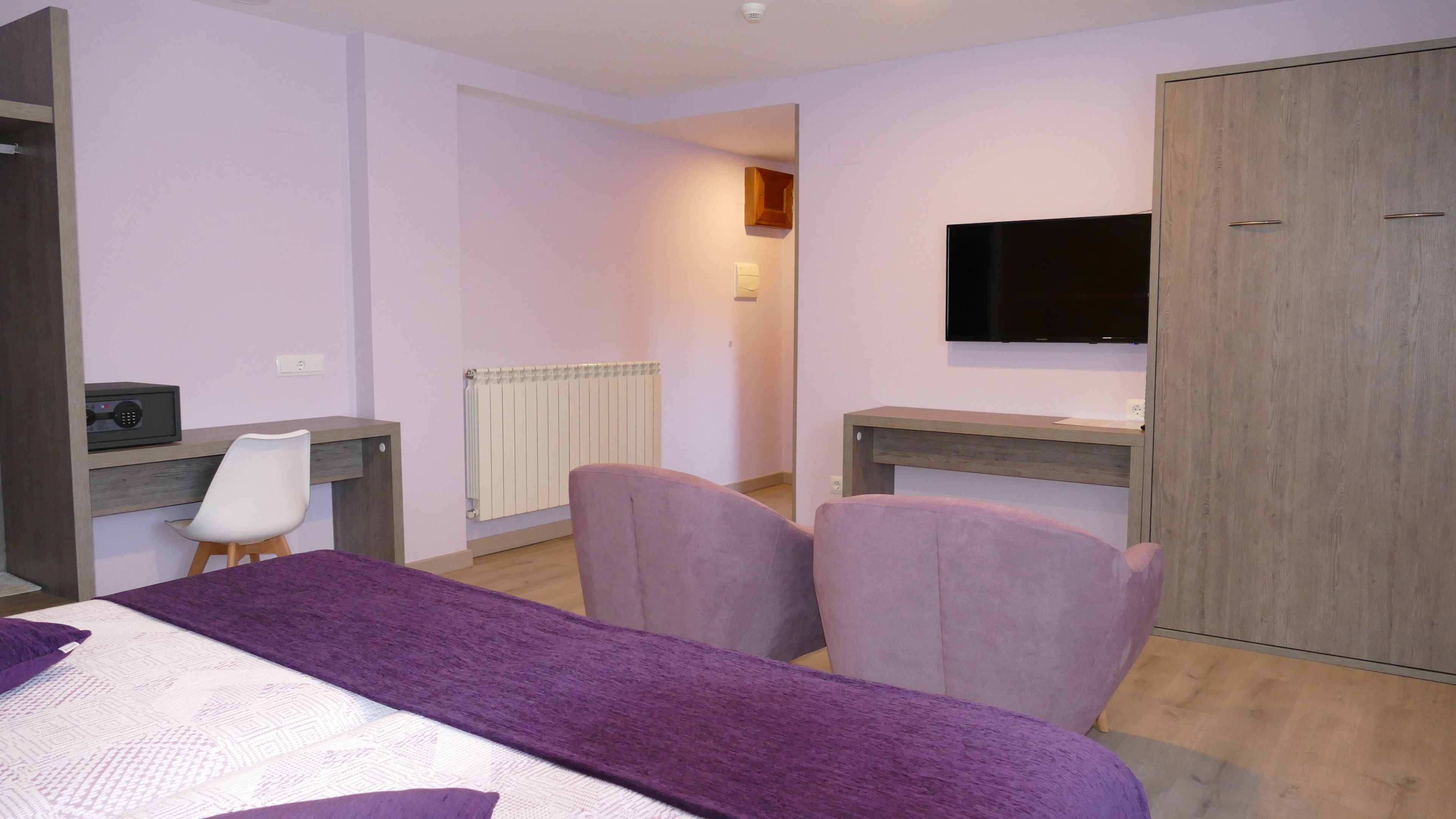 A hotel room with a bed, two chairs, a desk, a television, and a wardrobe.