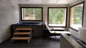 Une salle de spa équipée d’un bain à remous, de deux fauteuils et d’une petite étagère en bois.