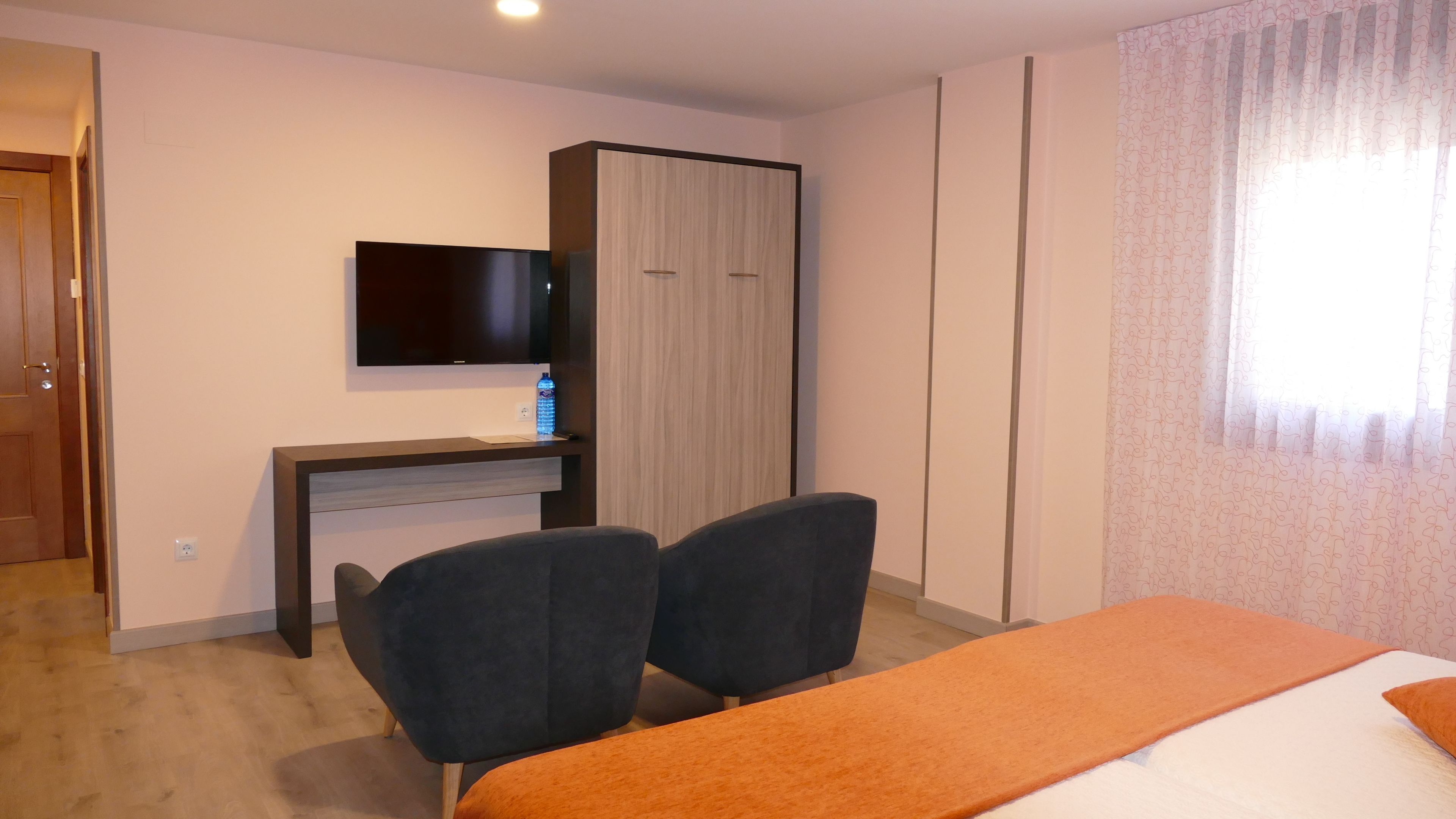 Una camera d'albergo con un letto, due sedie, una scrivania con televisore e un armadio.
