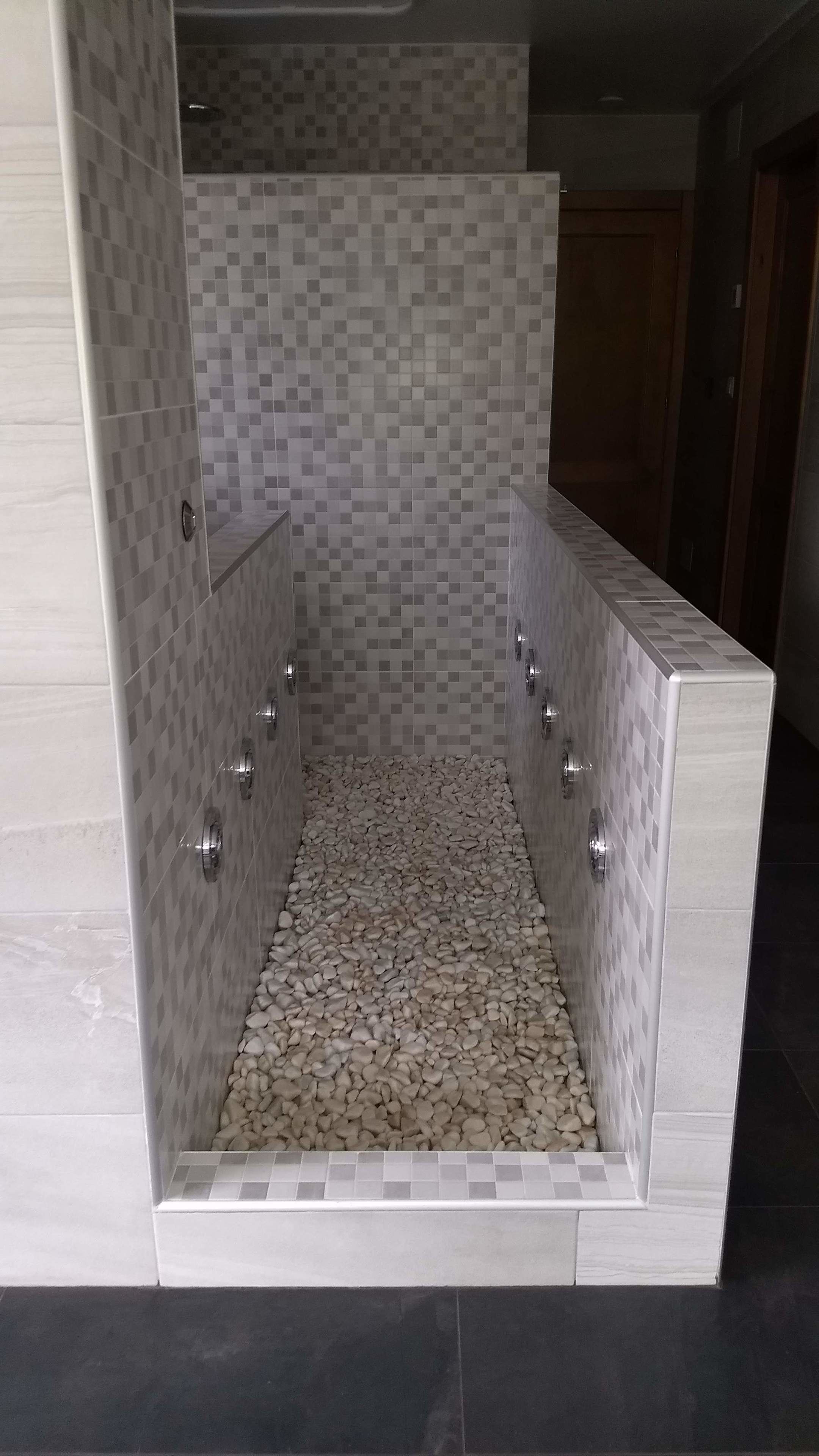 Un área de ducha moderna con paredes de mosaicos y suelo de guijarros.