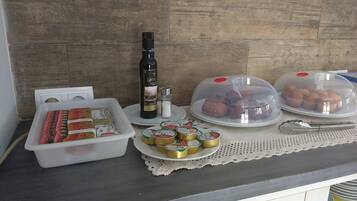 Una encimera de cocina con diversos alimentos, incluyendo una botella de vino, un recipiente con pan de la marca Helios y dos platos cubiertos de pasteles.