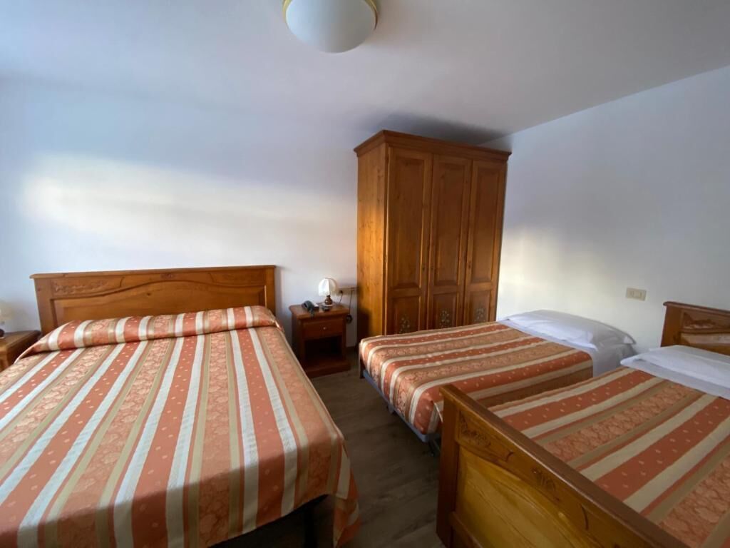 A room with two wooden beds, a wardrobe, and a nightstand with a lamp.