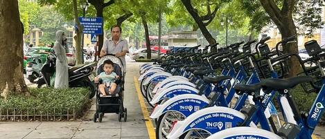 A row of blue and white TNG bicycles parked along a tree-lined sidewalk.