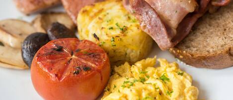 A breakfast plate with scrambled eggs, bacon, toast, roasted potatoes, and a grilled tomato.
