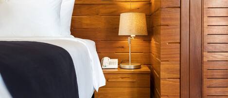 A neatly made bed with white linens, a bedside lamp, and a phone on a wooden nightstand.