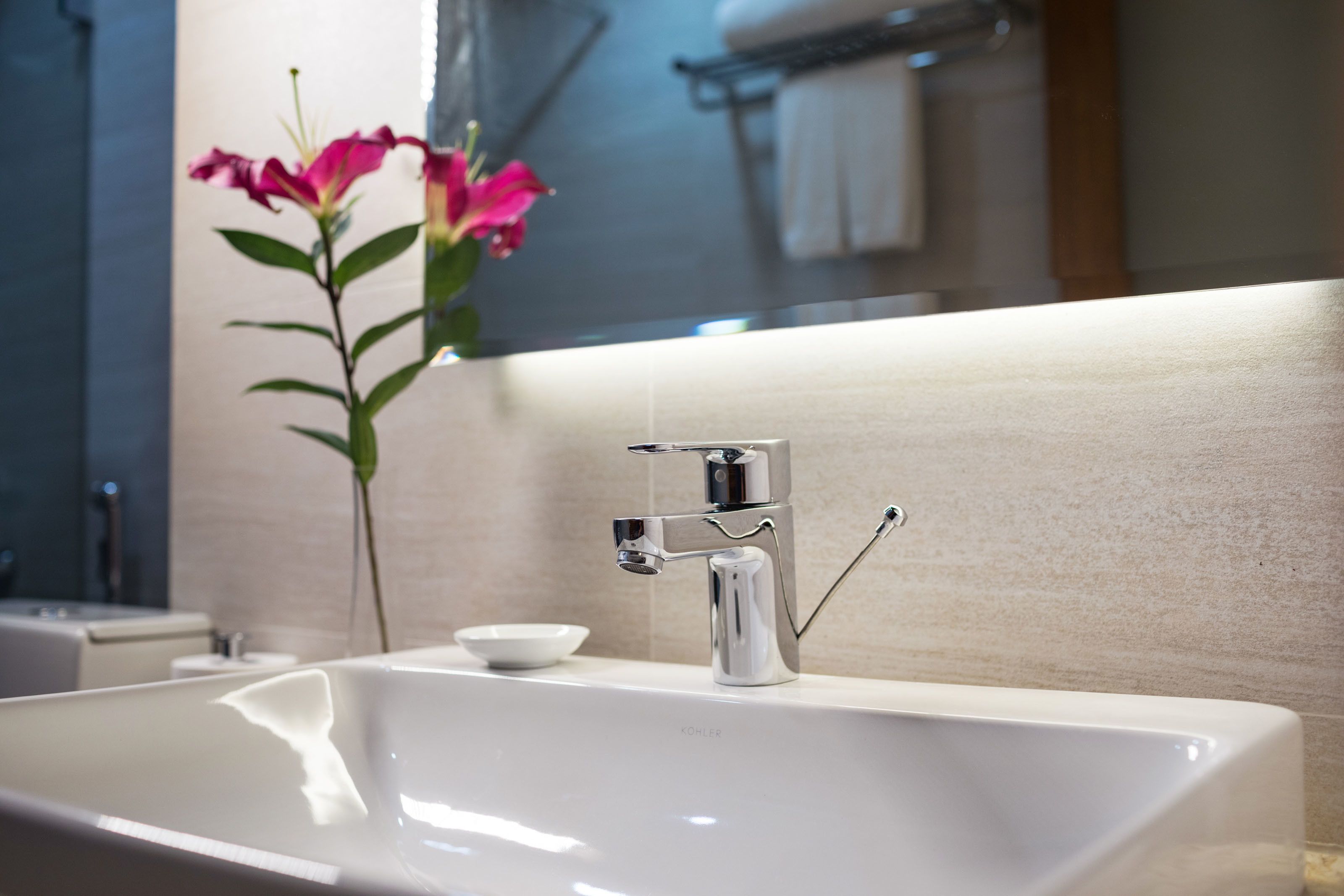 Un baño moderno con lavamanos blanco, grifo cromado y un florero con flores rosadas.