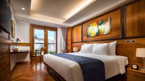 Una habitación de hotel con una cama grande, paneles de madera, un cuadro en la pared, un escritorio con una silla y una ventana con vistas a edificios.