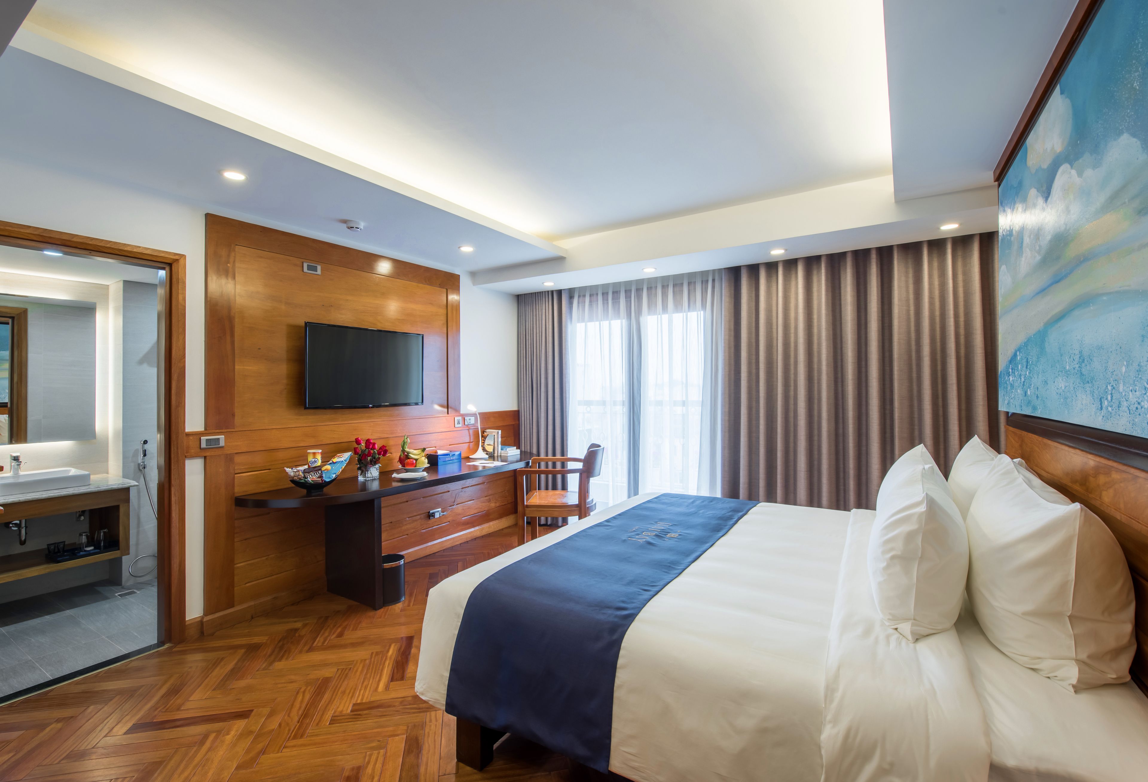 Una habitación de hotel con una cama grande, un escritorio de madera, un televisor de pantalla plana y un baño visible a través de una puerta abierta.