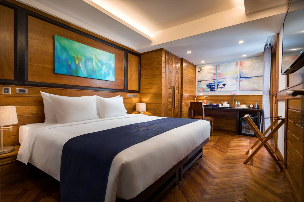 A hotel room with a large bed, wooden paneling, a desk with a chair, and artwork on the walls.