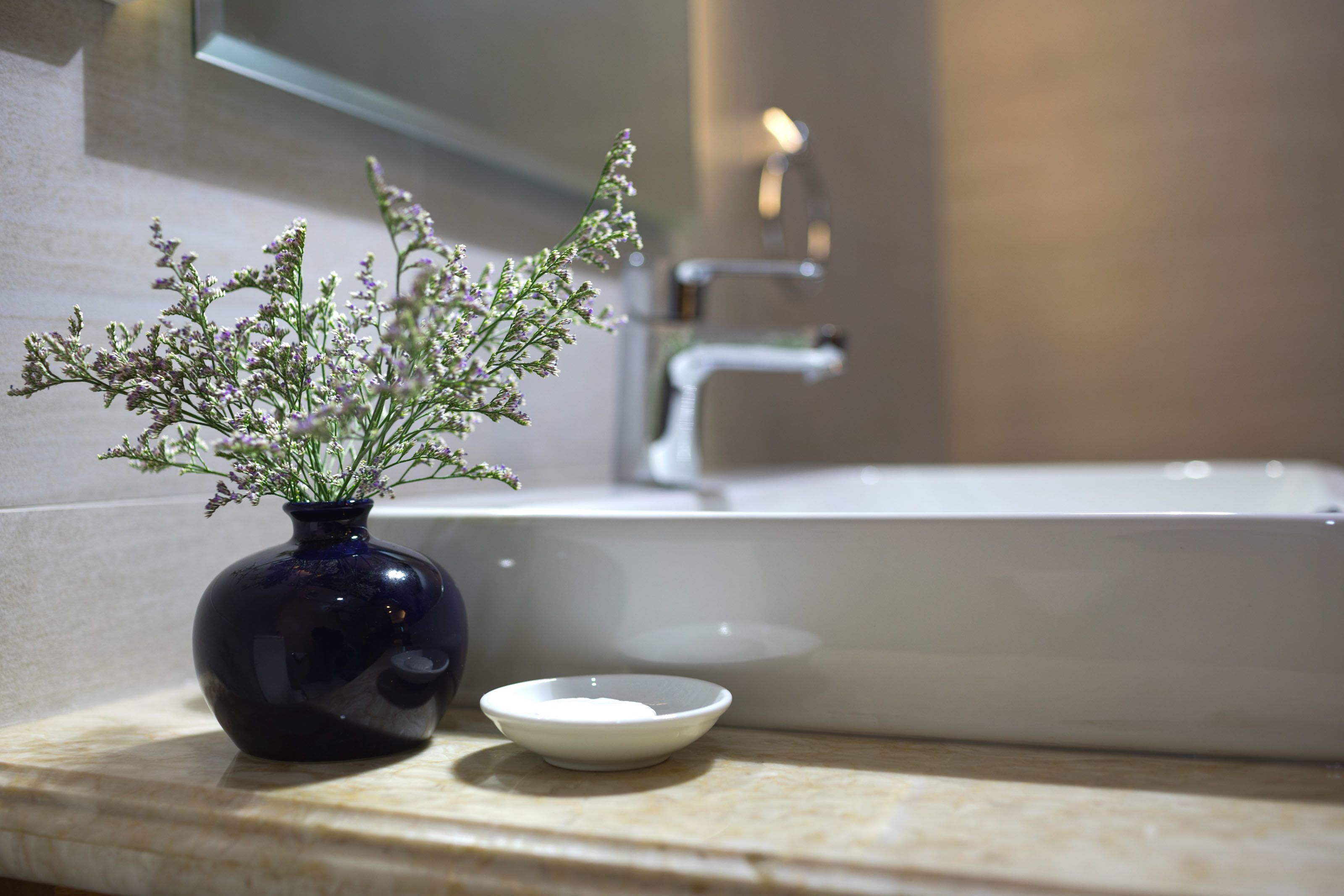 A bathroom with a dark blue vase containing flowers on the counter, a white sink, and a small white bowl.