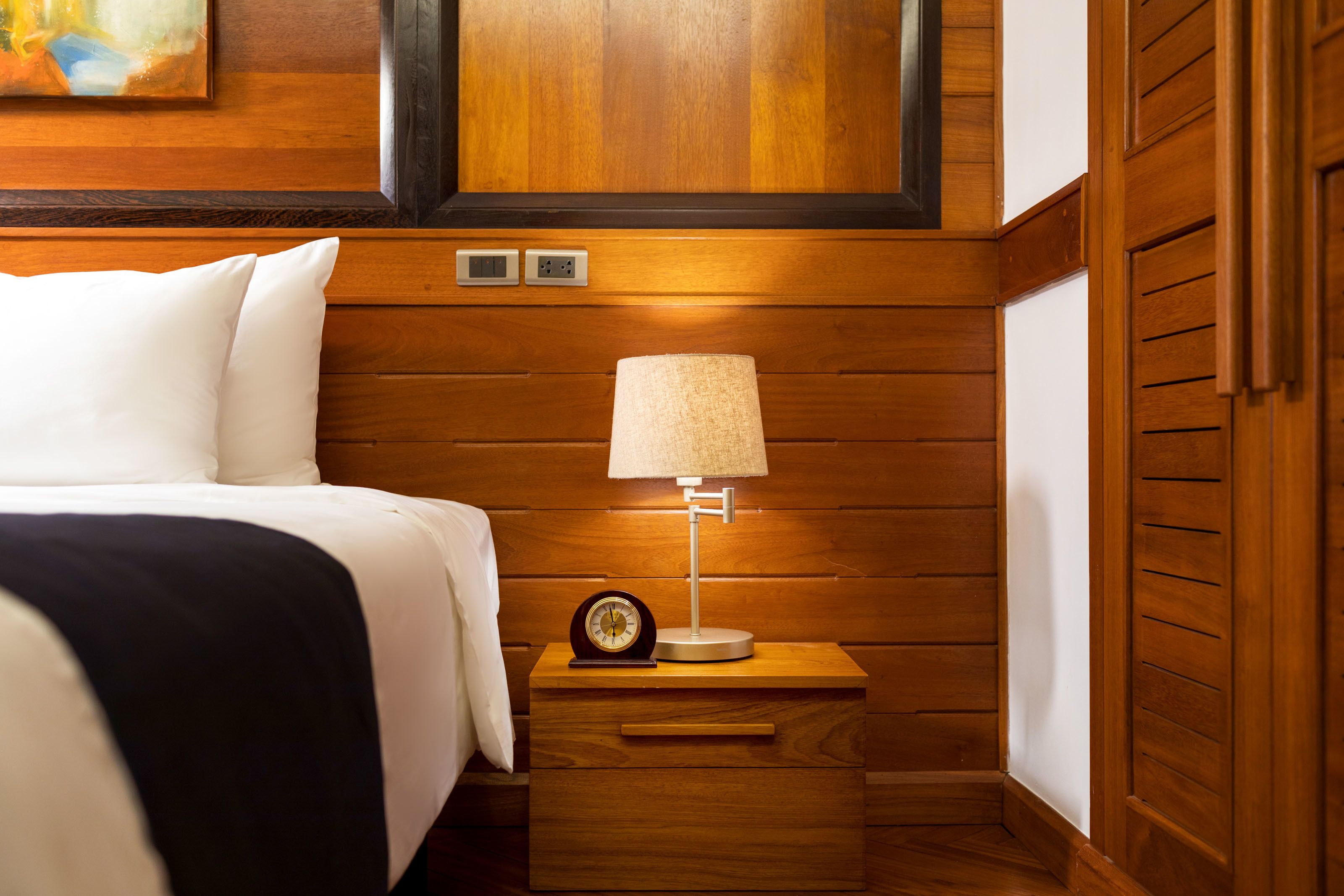 A neatly made bed with white linens, a bedside table with a lamp, and a clock.